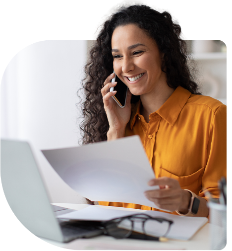Mulher sorrindo ao telefone enquanto lê papéis